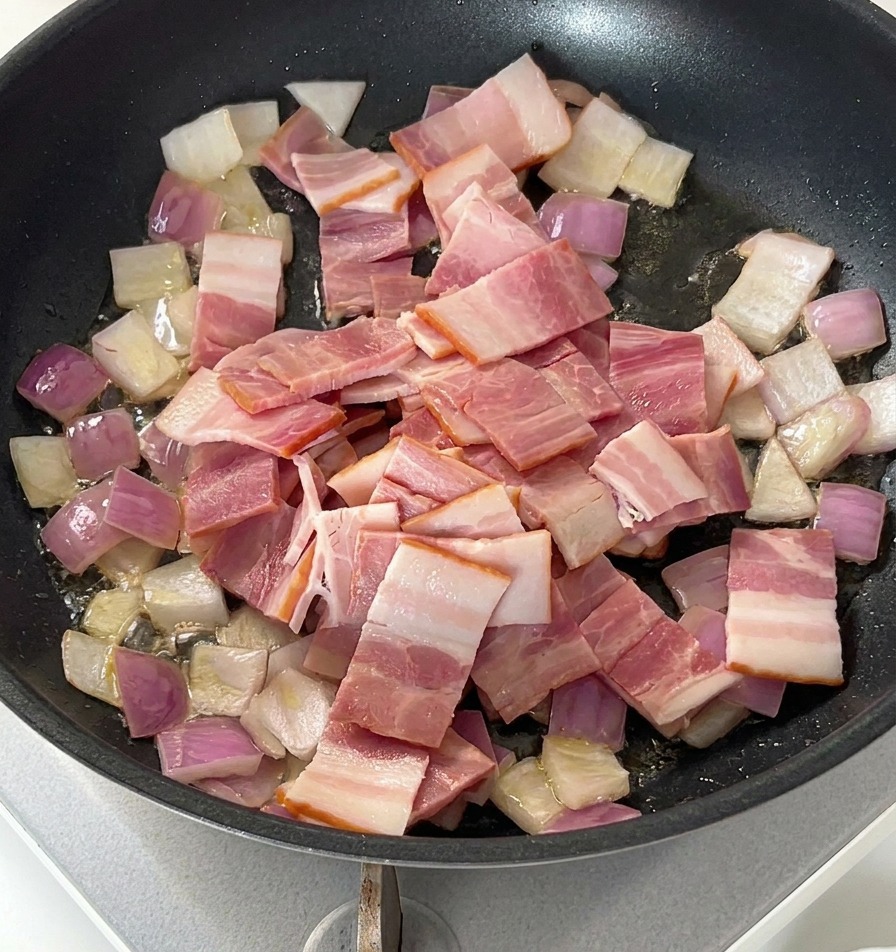 Morceaux de bacon cru posés sur des oignons revenus dans une poêle noire.