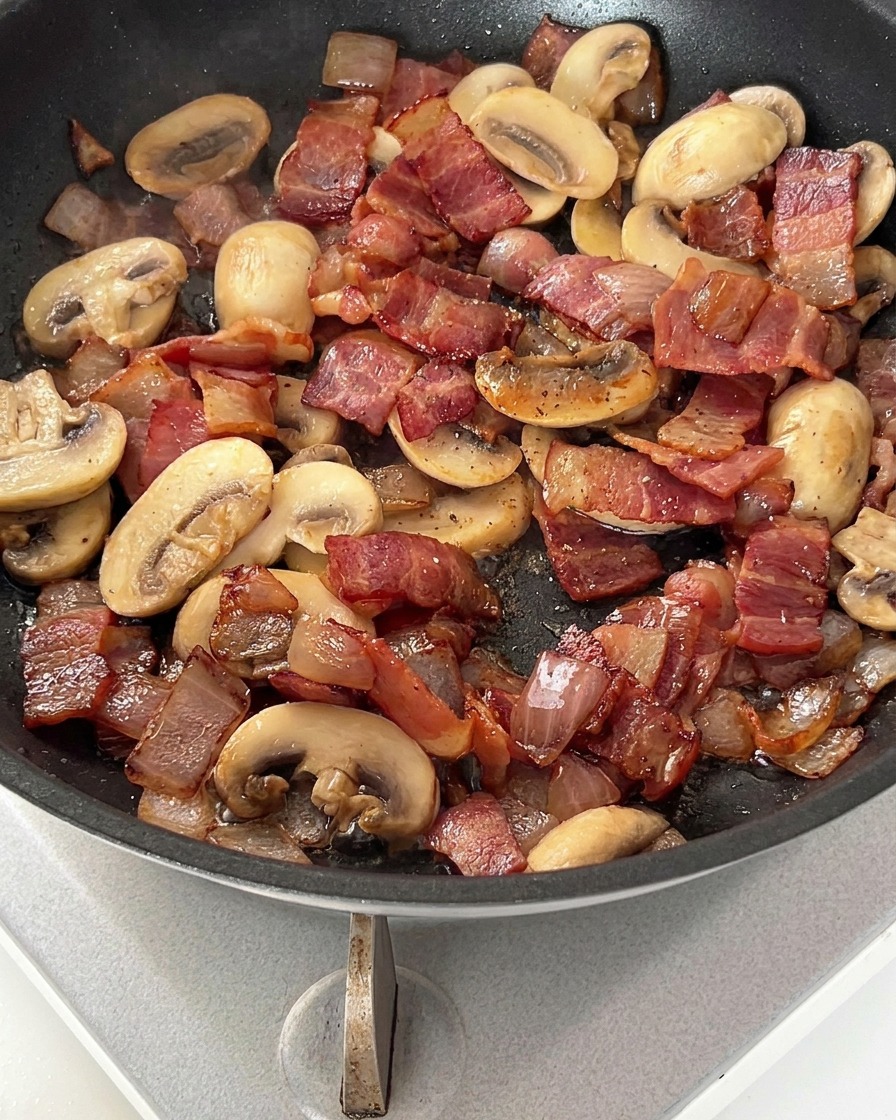Une poêle contenant du bacon, des oignons et des champignons parsemés de poivre noir.