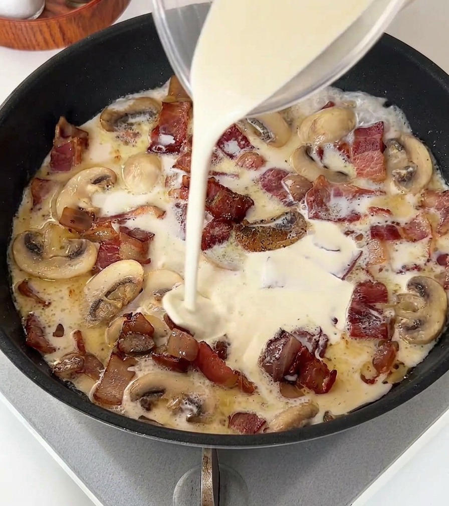 Un filet de crème légère versé dun verre doseur dans une poêle contenant du bacon et des champignons.