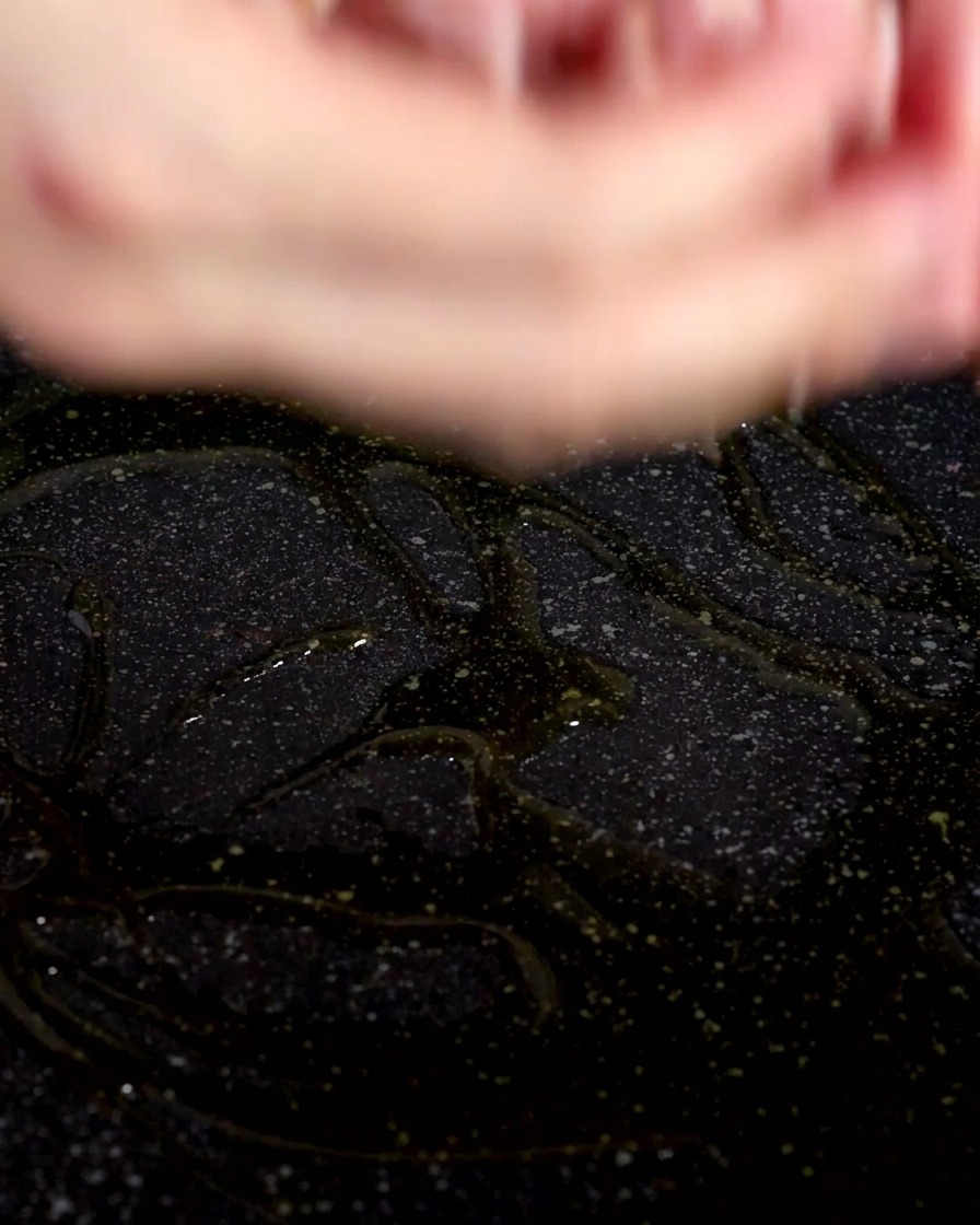 Gros plan de morceaux de bacon cru déposés dans une poêle sombre nappée dhuile dolive brillante.