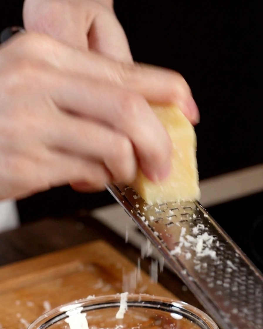 Une main utilisant une râpe métallique pour broyer un morceau de parmesan dur dans un bol.