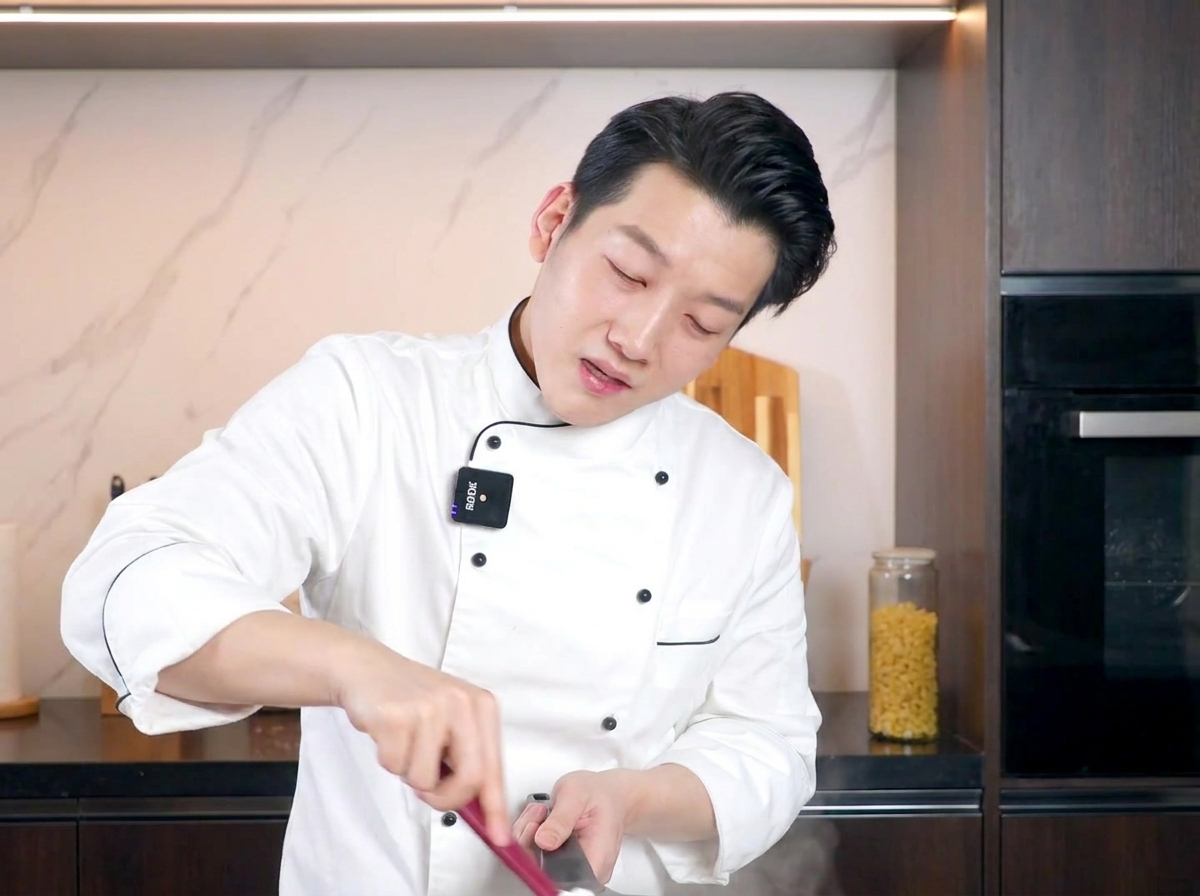Un chef remuant une poêle de pâtes crémeuses avec une spatule rouge, se concentrant sur le mélange de la sauce à lœuf.