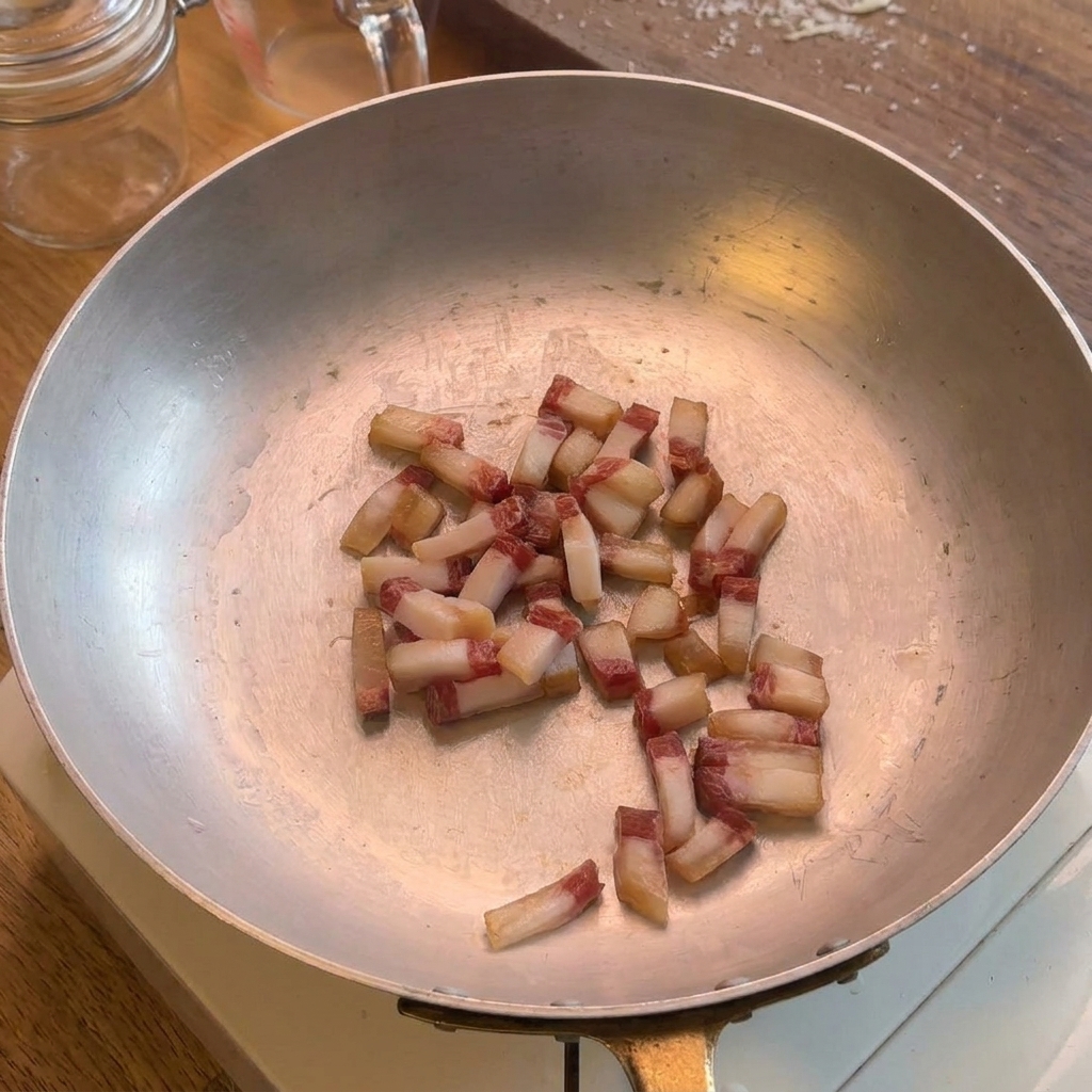 Petits dés de guanciale frémissant dans une poêle en inox, libérant leur gras naturel.