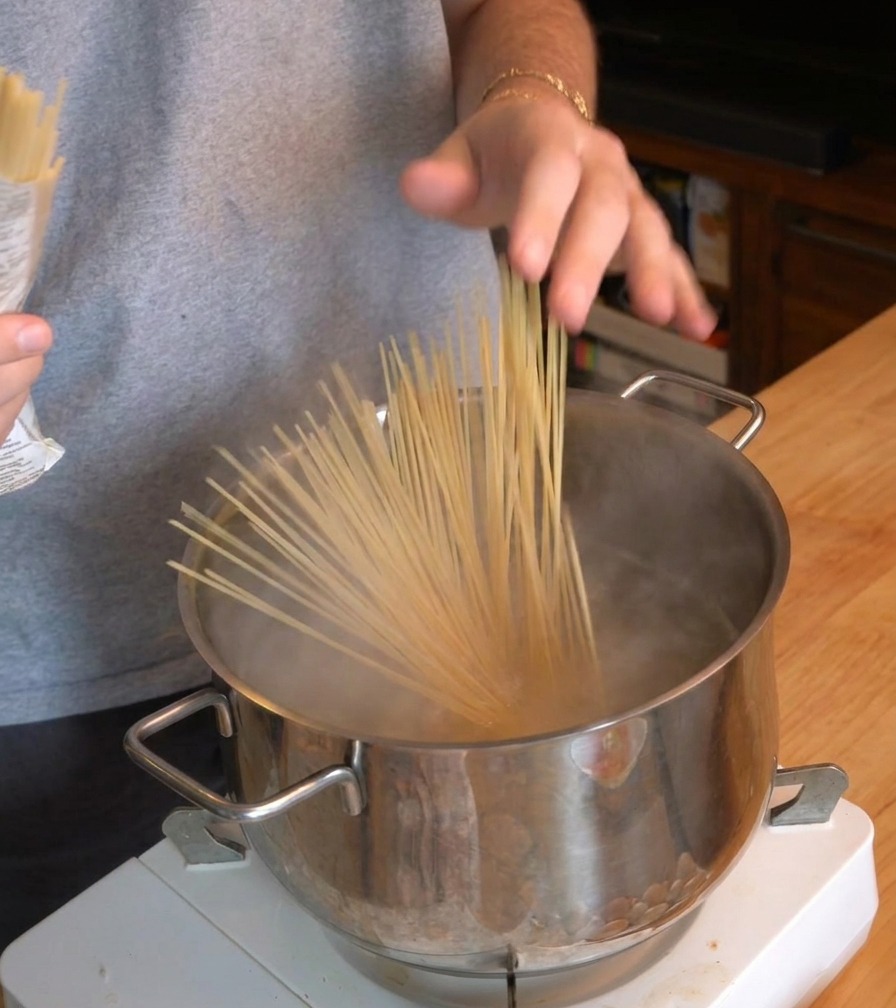Une personne plongeant un bouquet de spaghetti secs dans une casserole deau bouillante fumante.