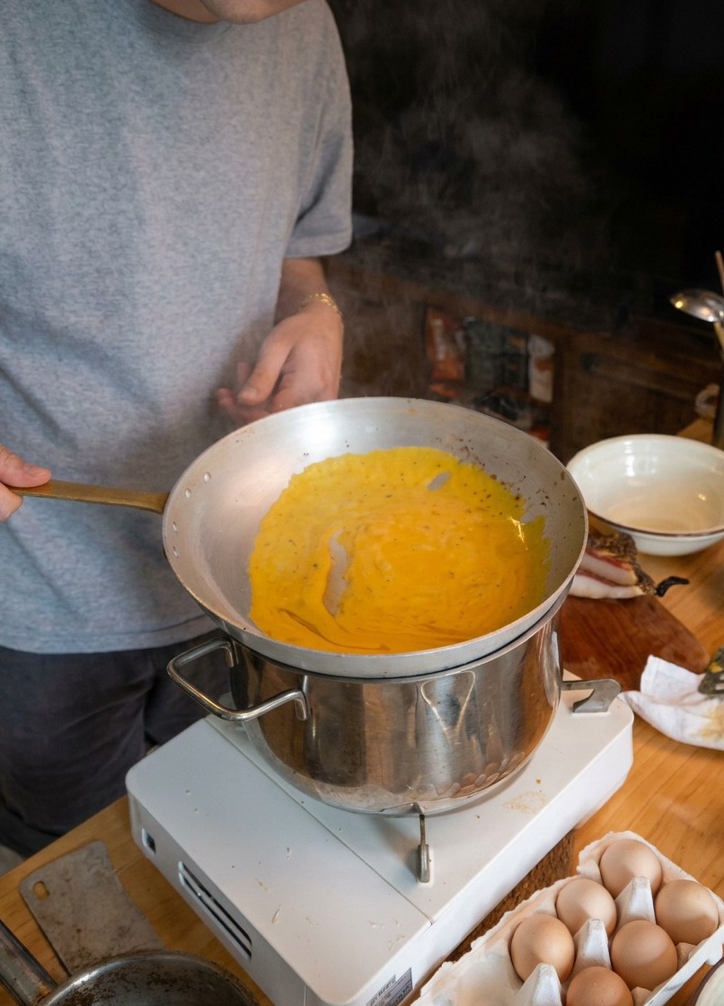 Un chef faisant sauter des spaghetti dans une poêle au-dessus dune casserole deau fumante.