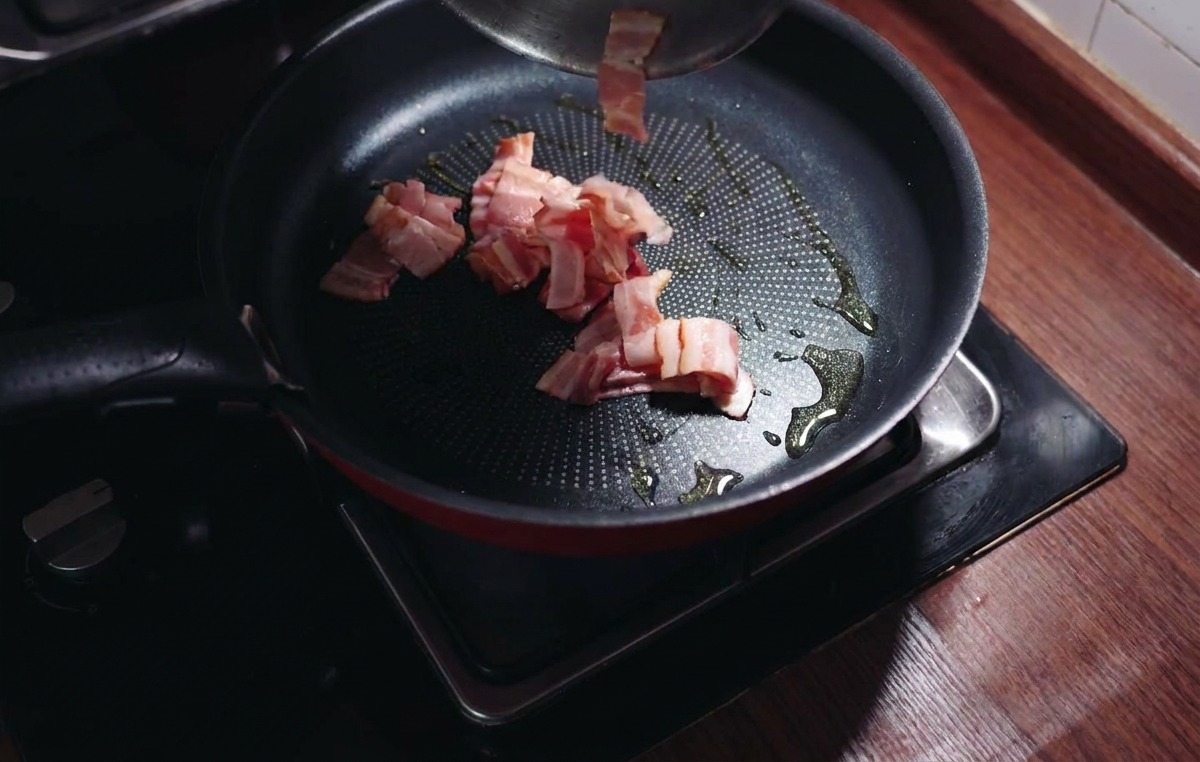 Morceaux de bacon hachés ajoutés dans une poêle chaude avec de lhuile dolive brillante.