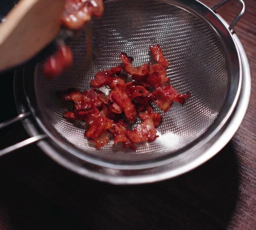 Bacon frit croustillant versé dans une passoire en acier inoxydable pour séparer le gras liquide.