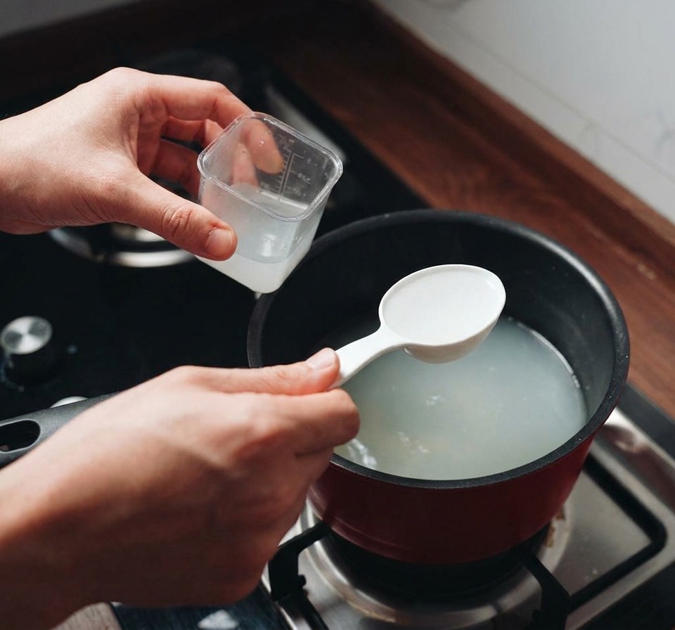 Une personne utilisant une louche blanche pour prélever leau trouble des pâtes dans une casserole fumante.