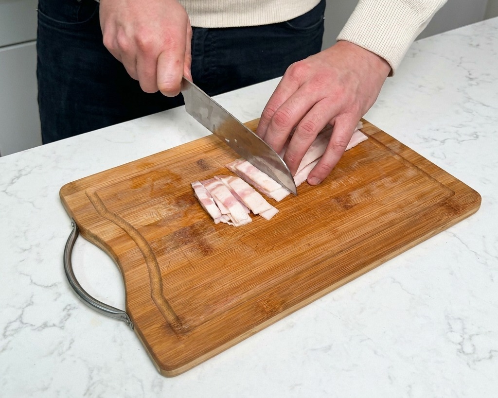 Découpe de tranches de bacon cru en petits rectangles sur une planche à découper.