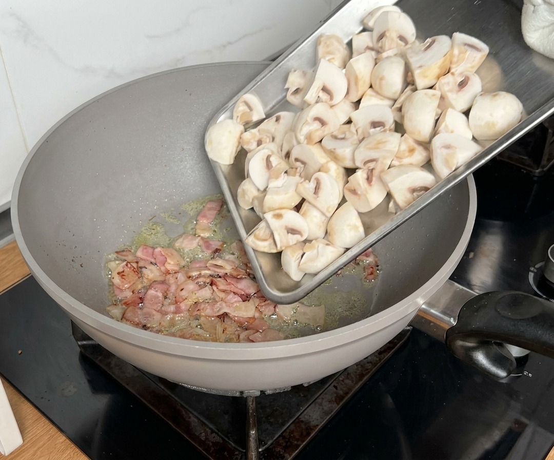 Champignons en quartiers ajoutés dans la poêle avec le bacon en cours de cuisson.