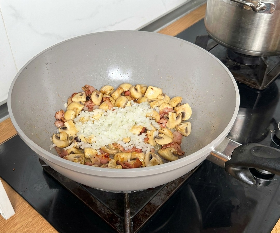 Oignons hachés placés au centre dune poêle avec le bacon et les champignons dorés.