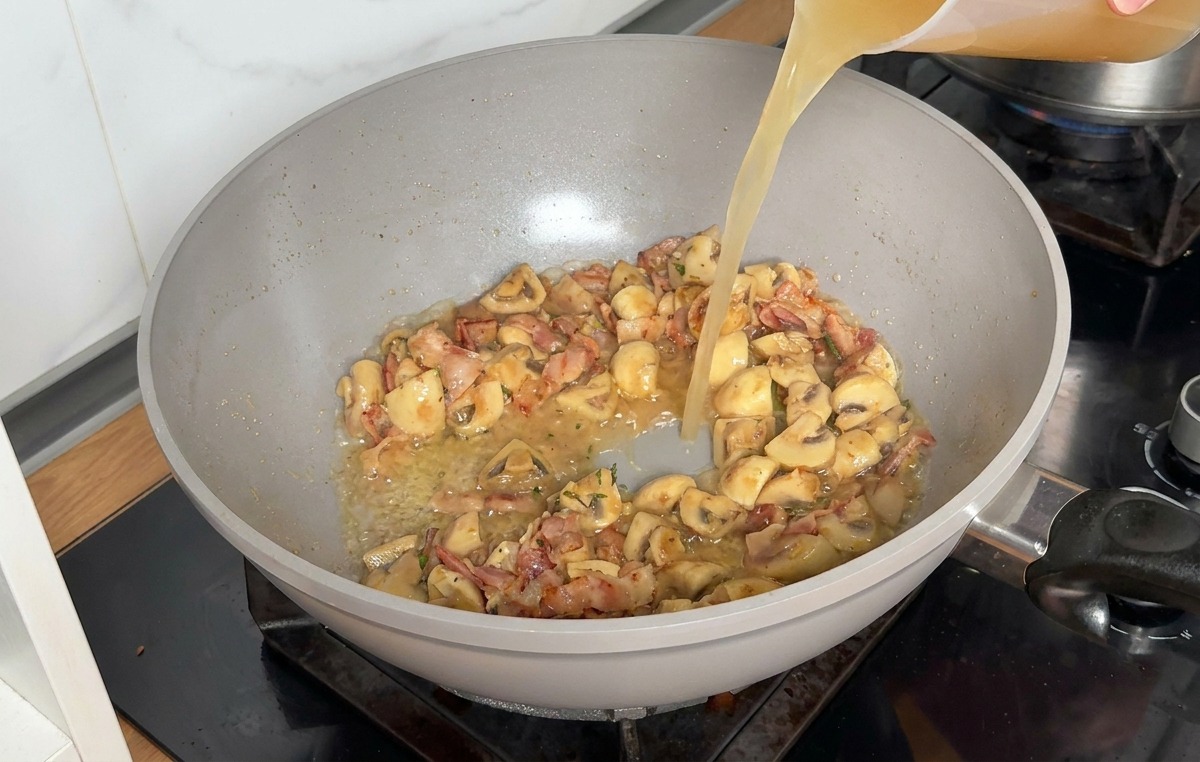 Bouillon de volaille versé dans la poêle avec les ingrédients sautés.
