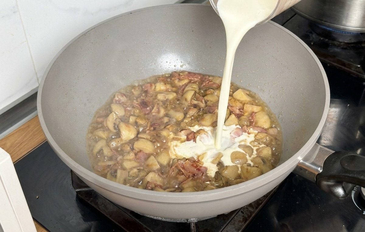 Crème liquide versée dans la poêle avec le bouillon réduit et les champignons.