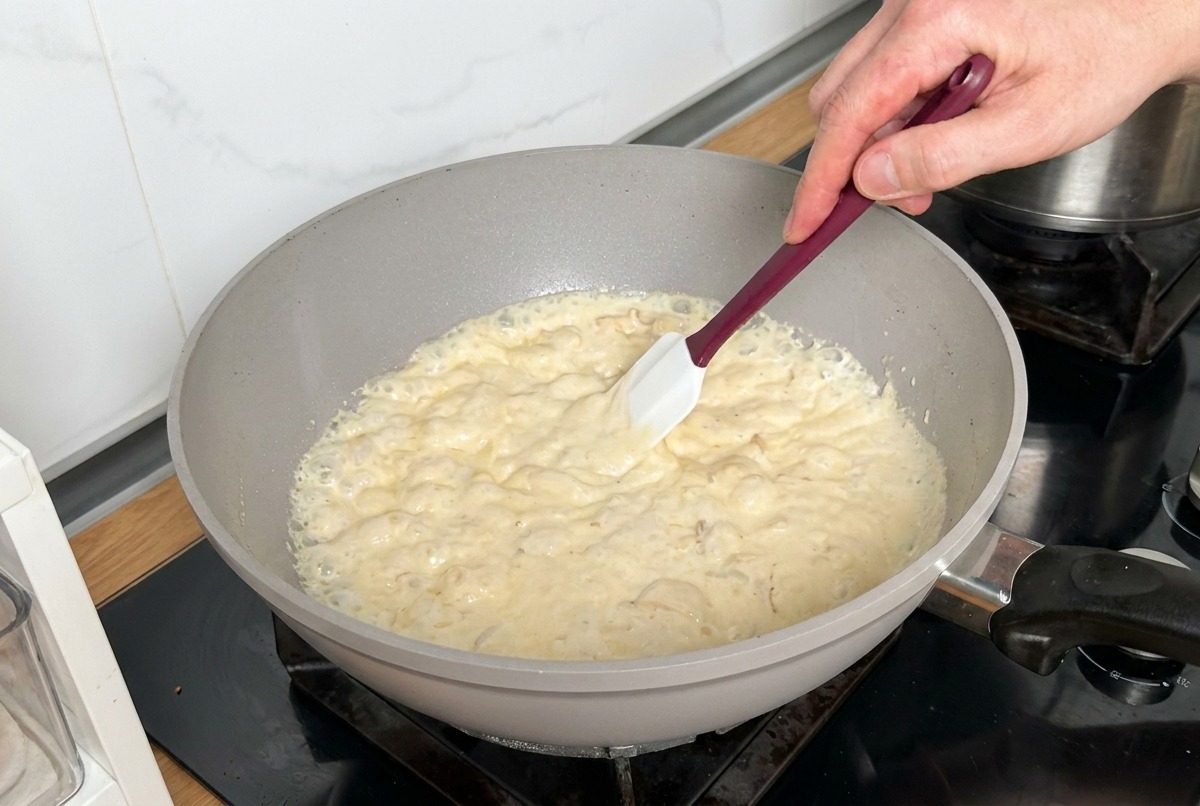 Une sauce crémeuse épaisse bouillonnante avec champignons et bacon remuée avec une spatule.