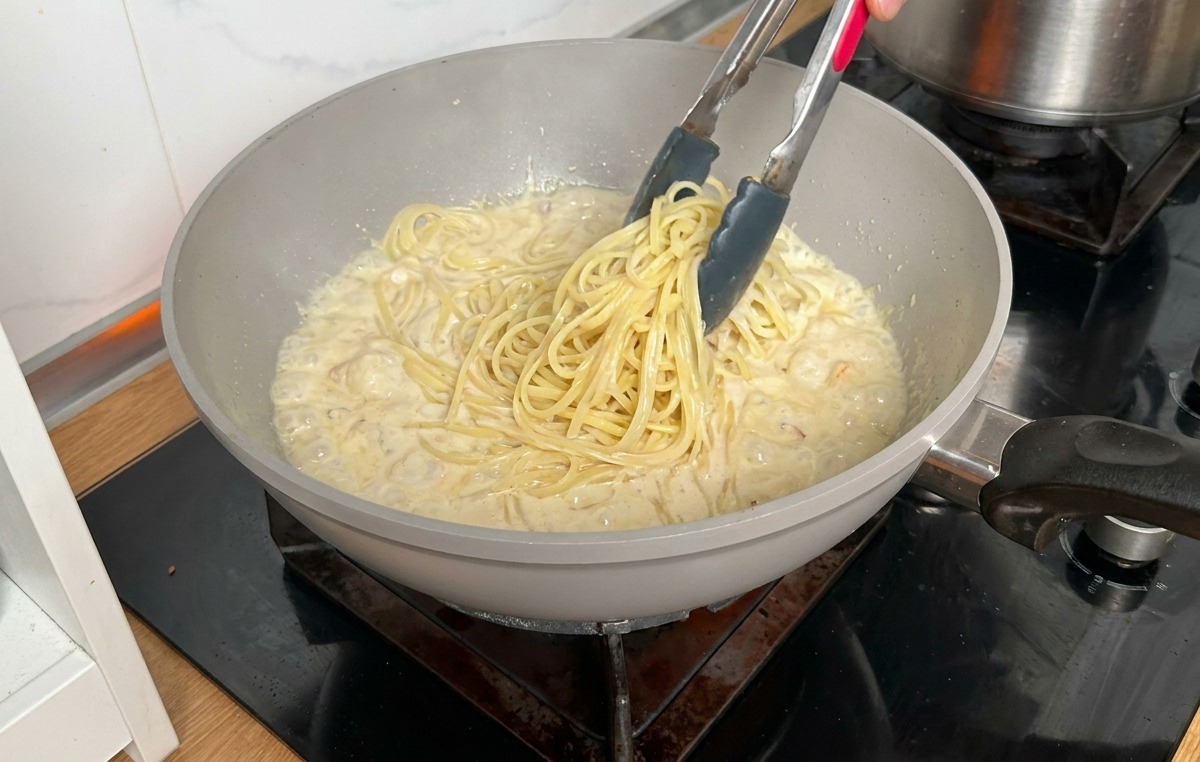 Pâtes cuites transférées avec une pince dune casserole vers la poêle de sauce crémeuse.