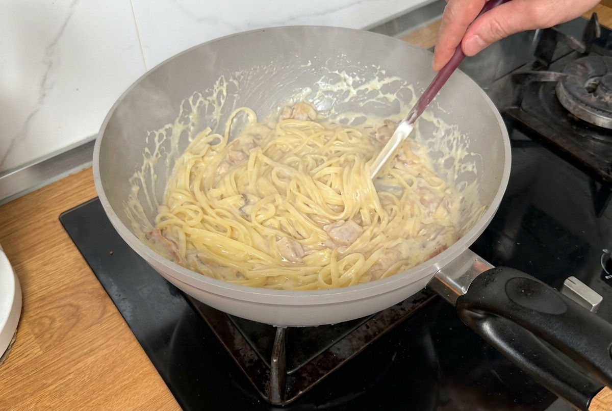 Pâtes mélangées dans une poêle avec une spatule pour assurer un enrobage uniforme de sauce.
