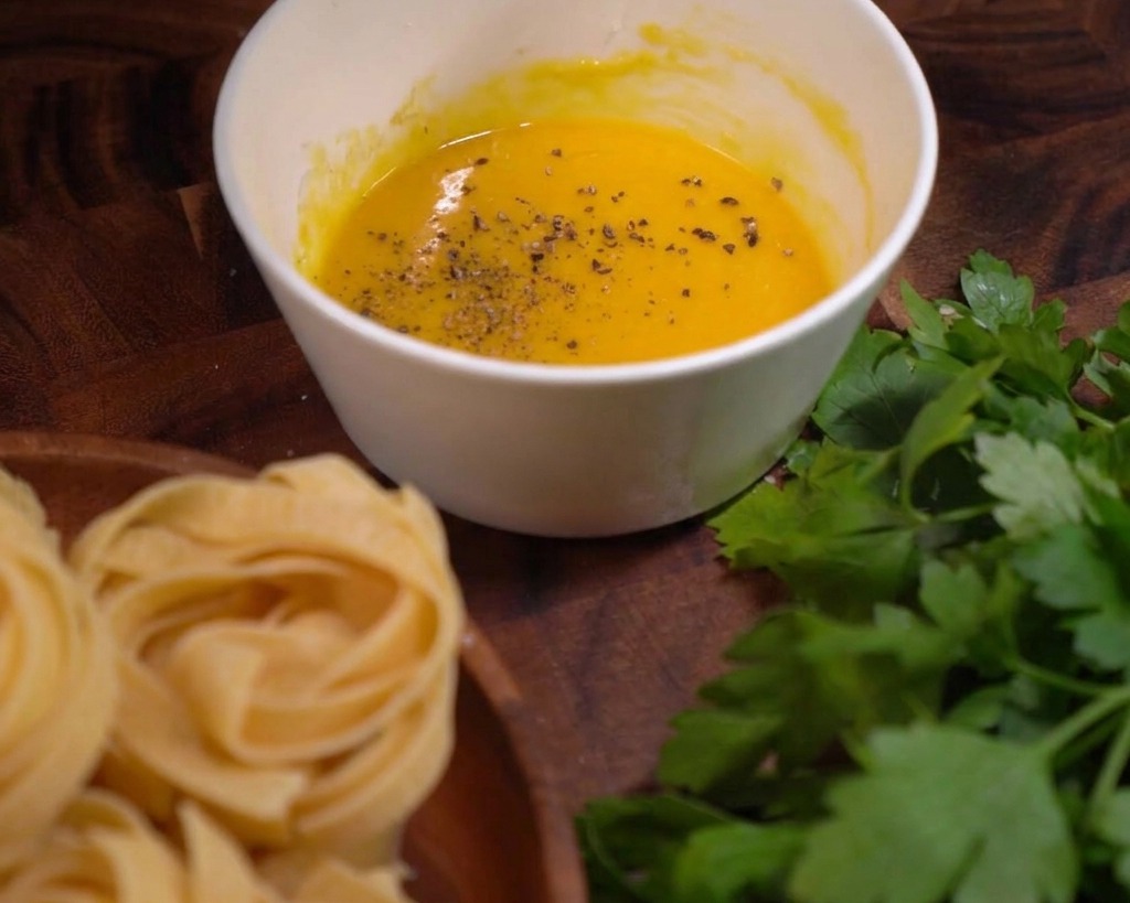 Grains de poivre noir concassés parsemant une sauce onctueuse aux œufs et au fromage dans un bol blanc.
