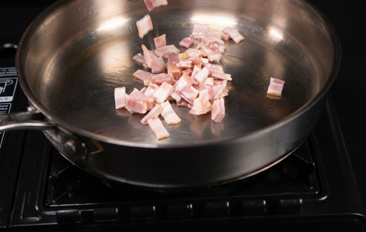 Petits morceaux de bacon déposés dans une poêle en inox bien chaude.