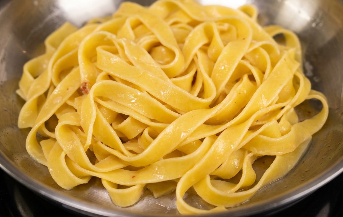 Fettuccine ajoutées dans une poêle en inox contenant le bacon doré et son gras de cuisson.