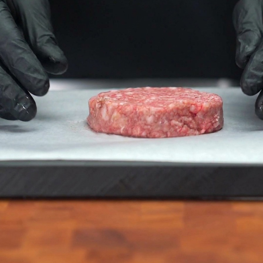 Un steak de bœuf haché cru posé sur du papier sulfurisé avec des grains de poivre noir visibles à sa surface.