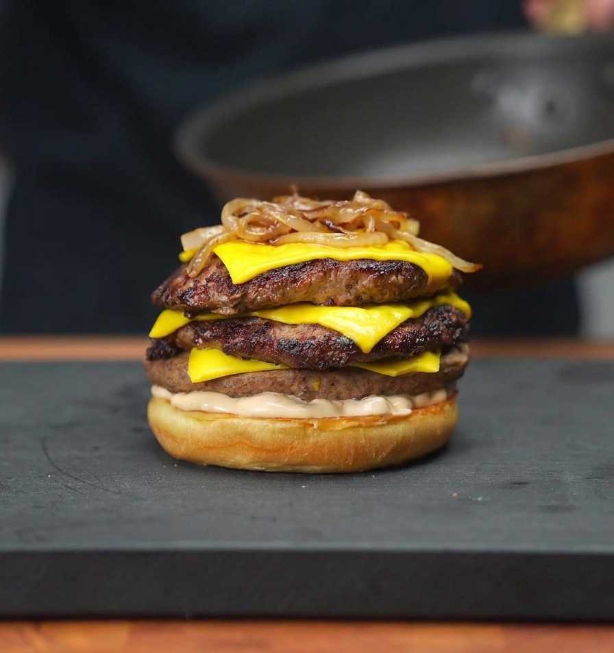 Des oignons caramélisés déposés sur une pile de steaks au fromage à laide de baguettes.