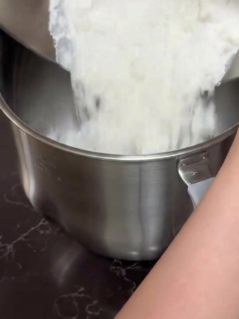 Mains versant le mélange de farine et de lait dans la cuve dun grand robot pâtissier.