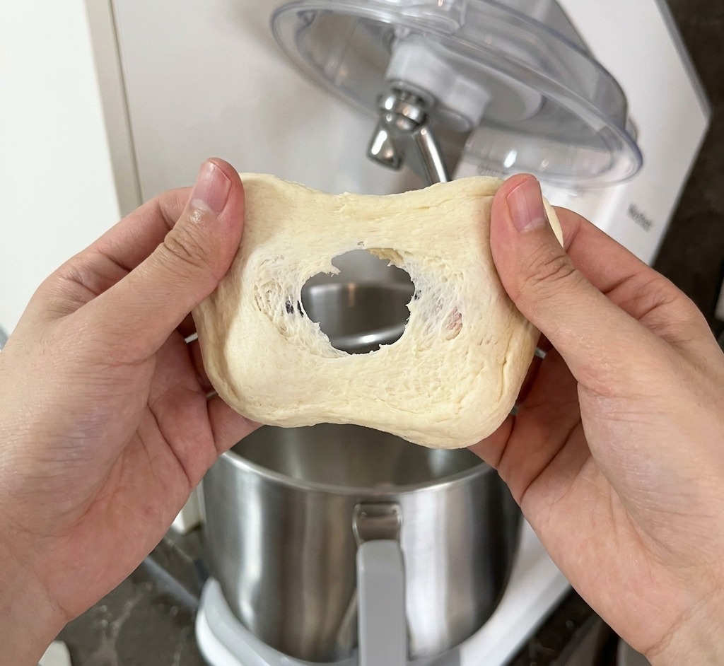 Une personne étirant un morceau de pâte pâle entre ses mains pour vérifier la formation dune membrane de gluten.