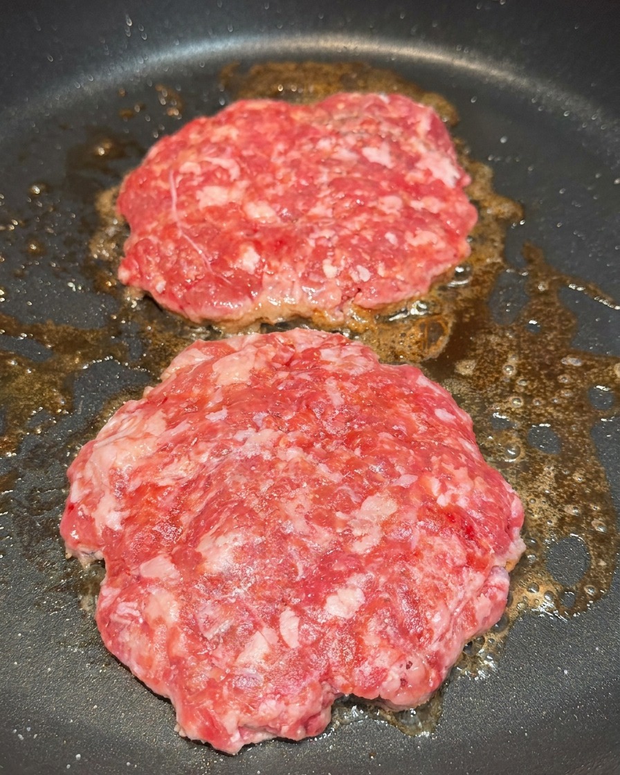Deux steaks de bœuf en cours de cuisson assaisonnés avec des grains de sel et de poivre noir.