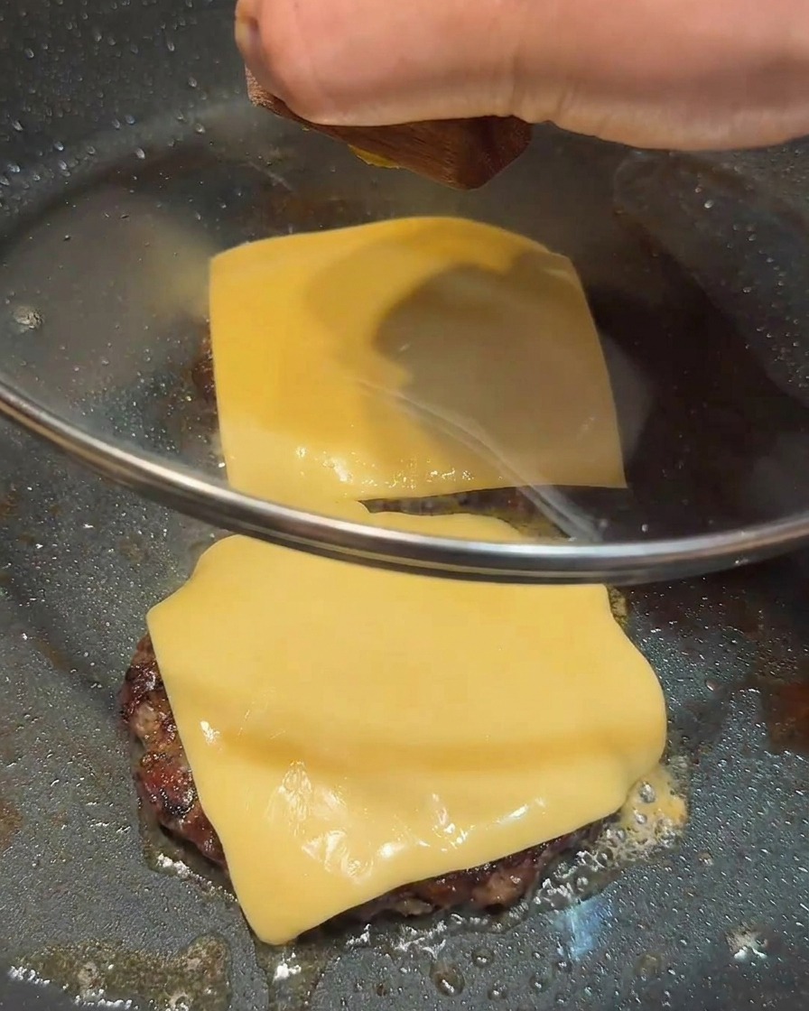 Couvercle en verre recouvrant la poêle contenant les deux steaks garnis de fromage.