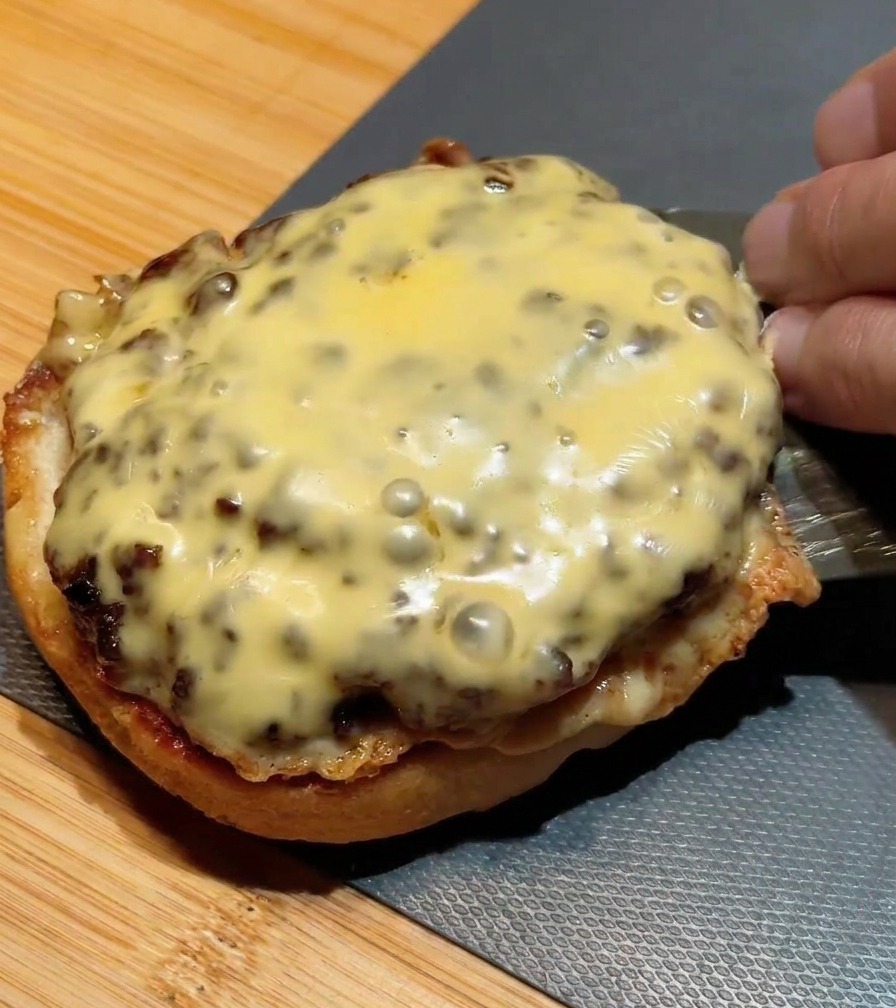 Spatule métallique empilant un second steak au fromage sur un premier déjà placé sur le pain.