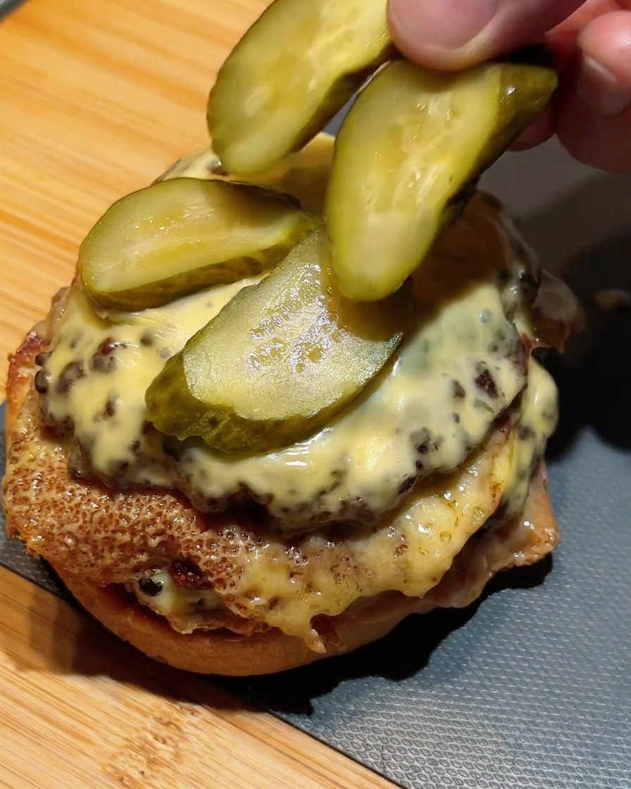 Disposition de rondelles de cornichons verts sur le double steak au fromage fondu.