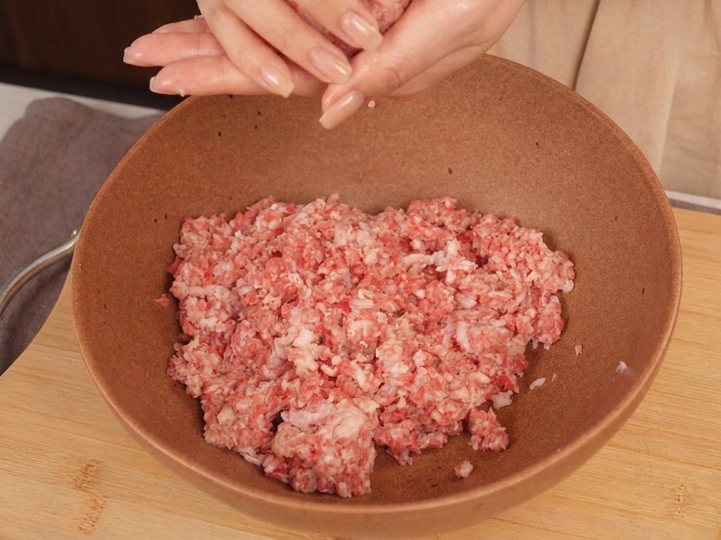 Mains dune personne formant une boule de bœuf haché cru au-dessus dun bol en céramique.