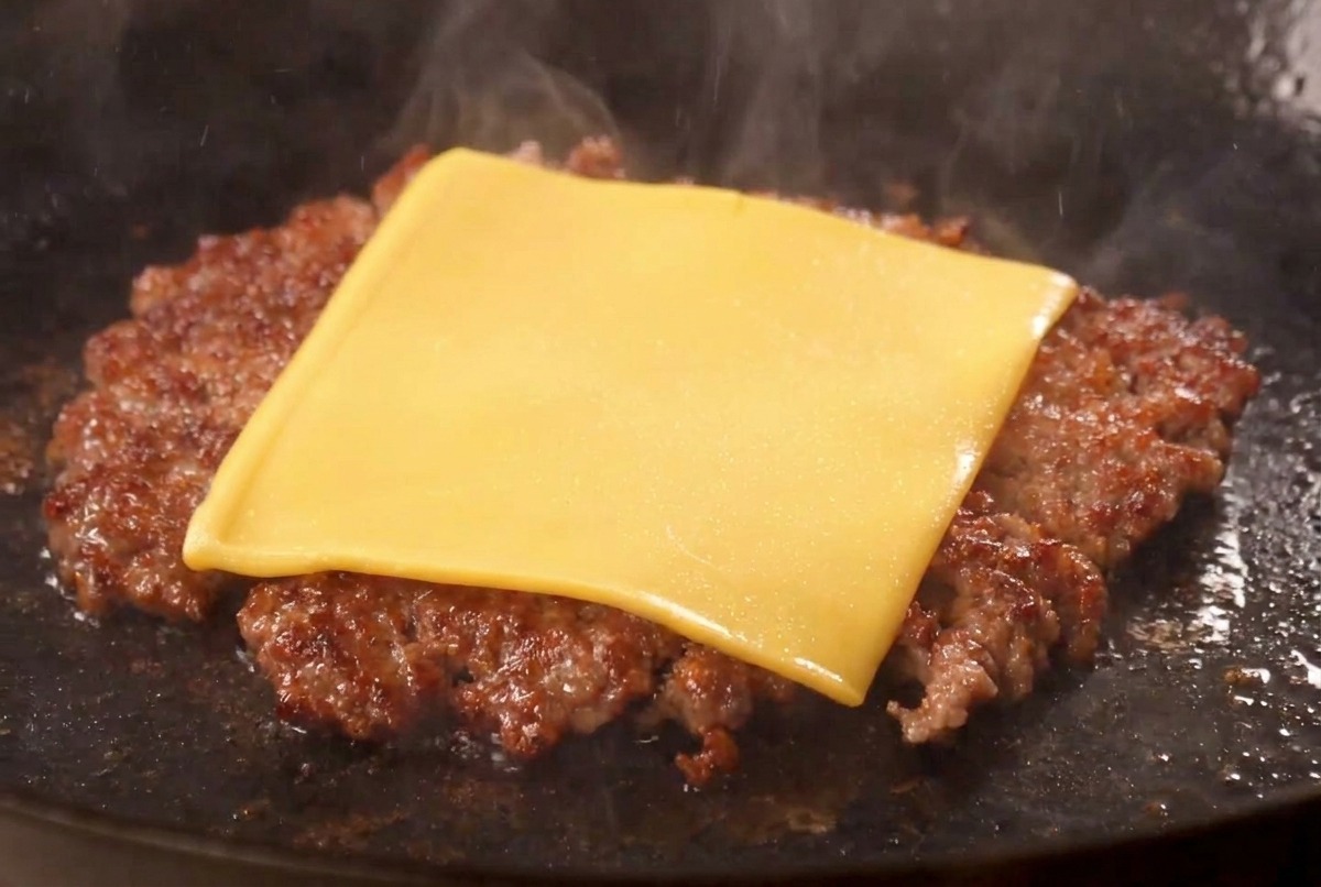Une tranche de fromage américain jaune fondant sur le dessus dun steak de bœuf saisi et croustillant dans une poêle.