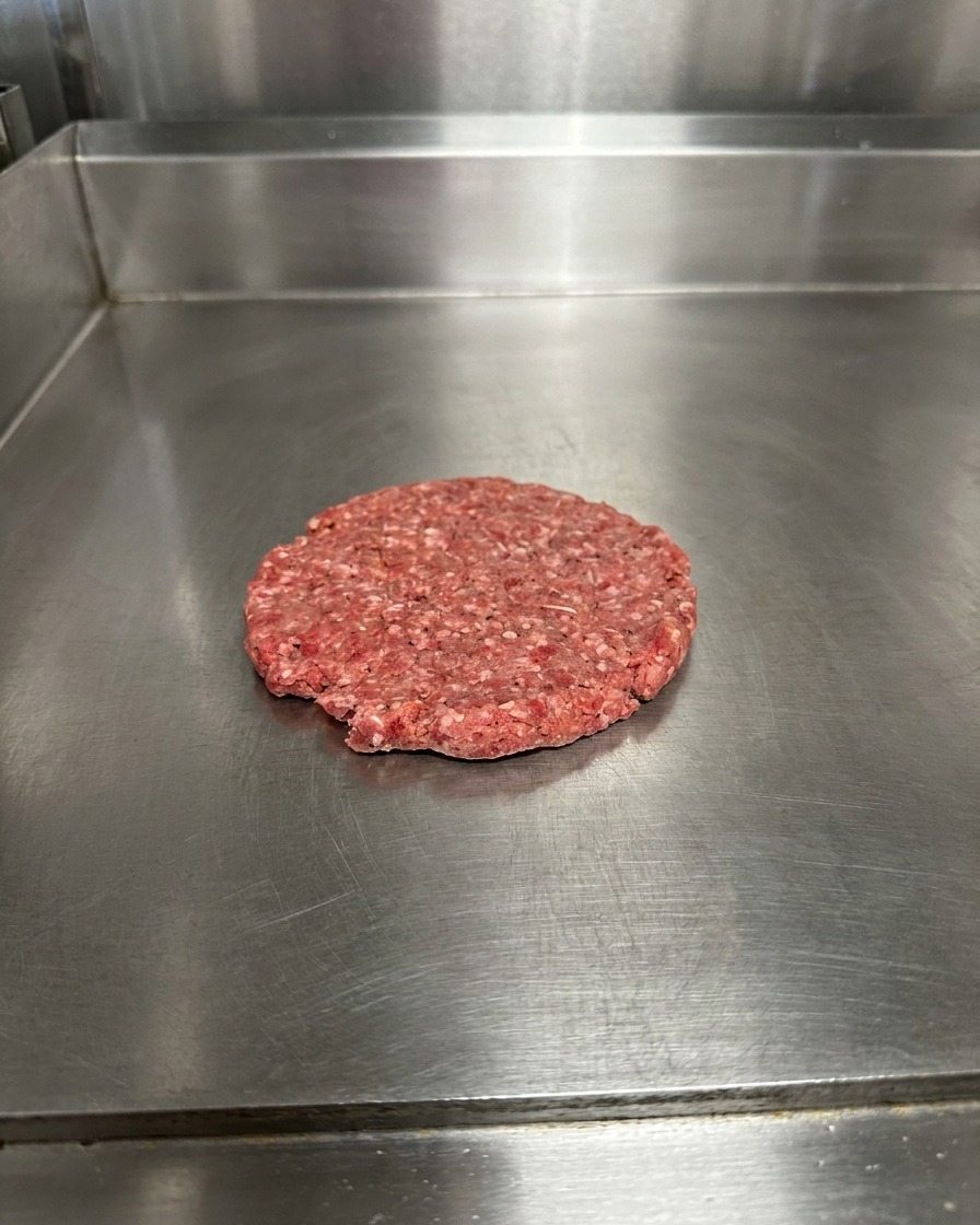 Un steak de bœuf aplati sur une surface métallique, assaisonné de gros grains de sel et de poivre.