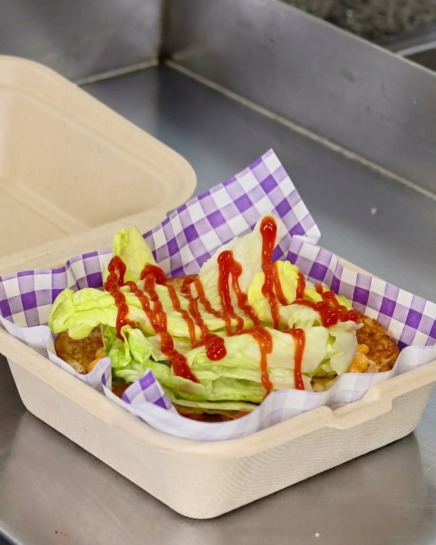 Tranches de tomate rouge et un steak de cheeseburger cuit empilés sur de la laitue dans un pain toasté.
