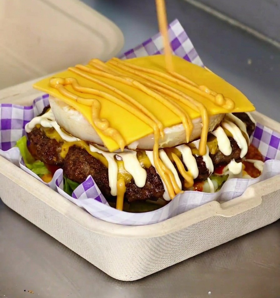 Un burger gourmet terminé avec un œuf au plat visible et du fromage fondu entre deux pains briochés toastés.