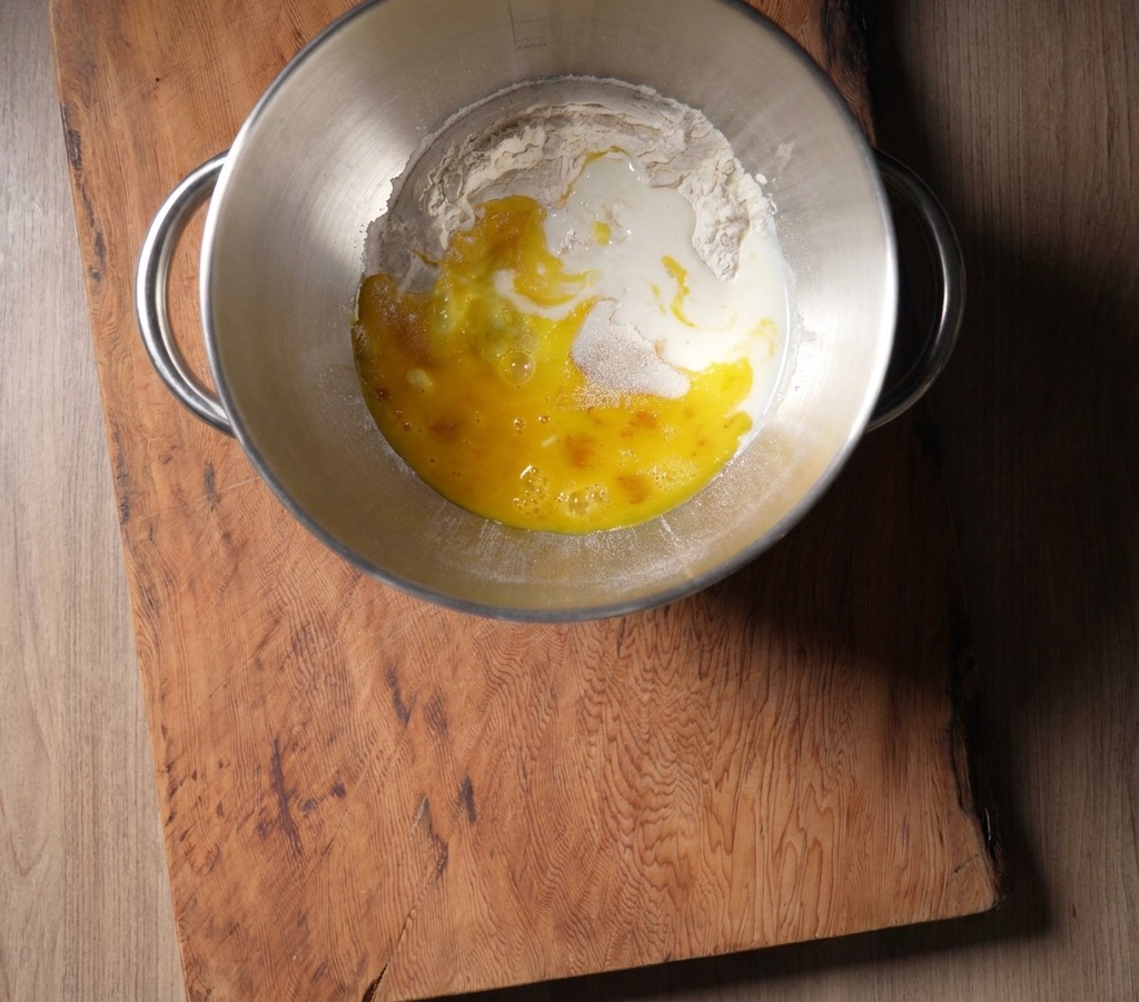 Lait frais versé sur le mélange de farine et dœufs dans une cuve de mixage en inox.