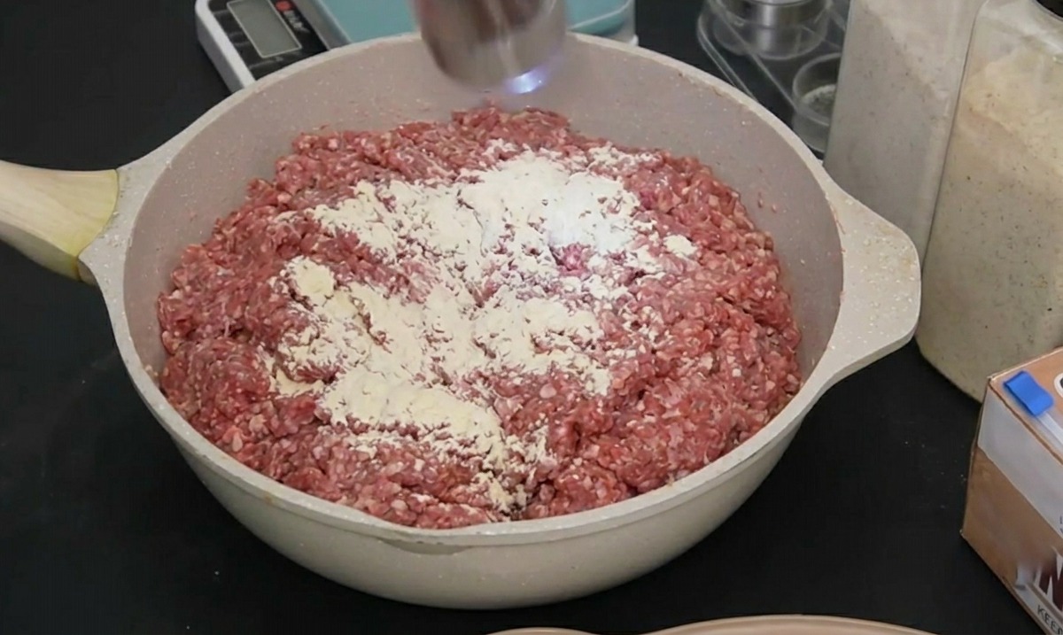 Un moulin à épices électrique en acier inoxydable moulant du poivre noir sur de la viande hachée crue assaisonnée.
