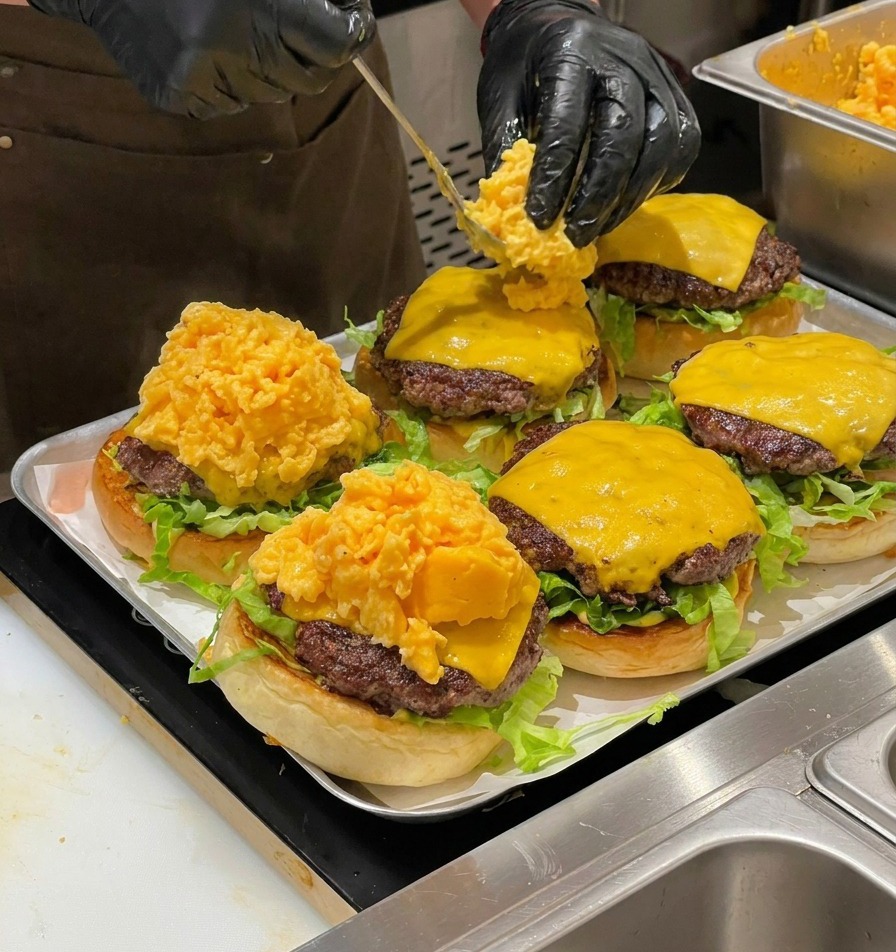 Chef utilisant une cuillère pour déposer une grande portion dœufs brouillés soyeux sur des cheeseburgers.