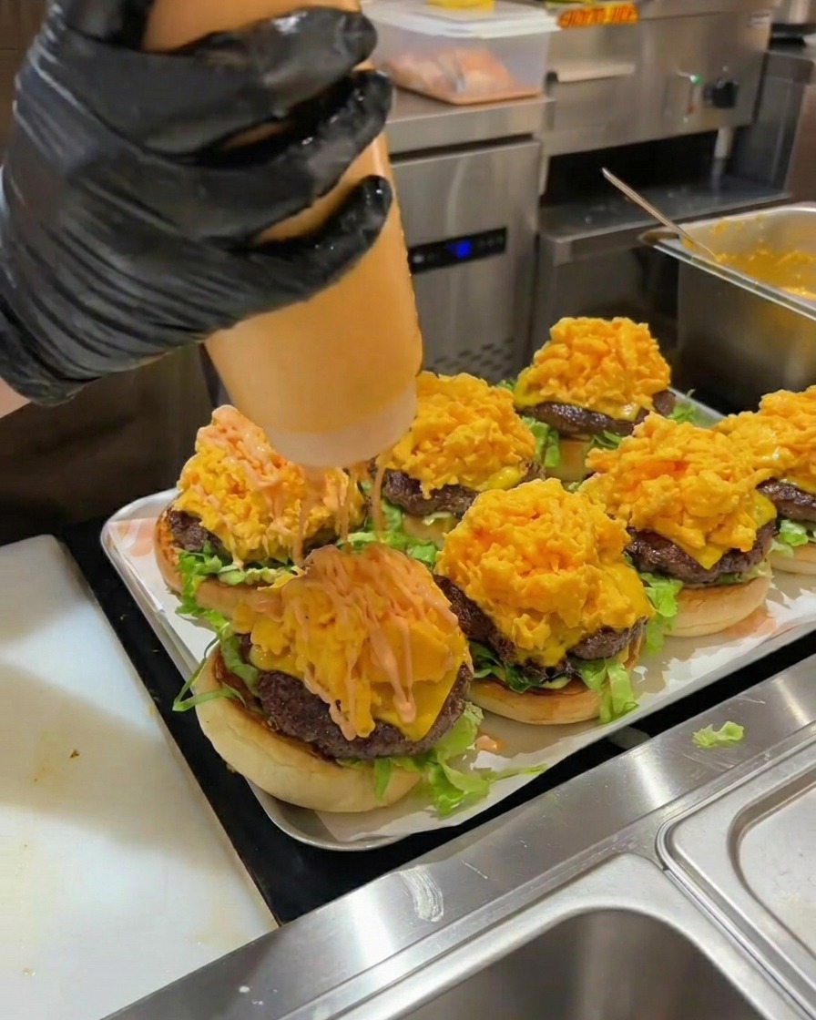 Sauce burger orange versée sur une pile dœufs brouillés dans un burger assemblé.