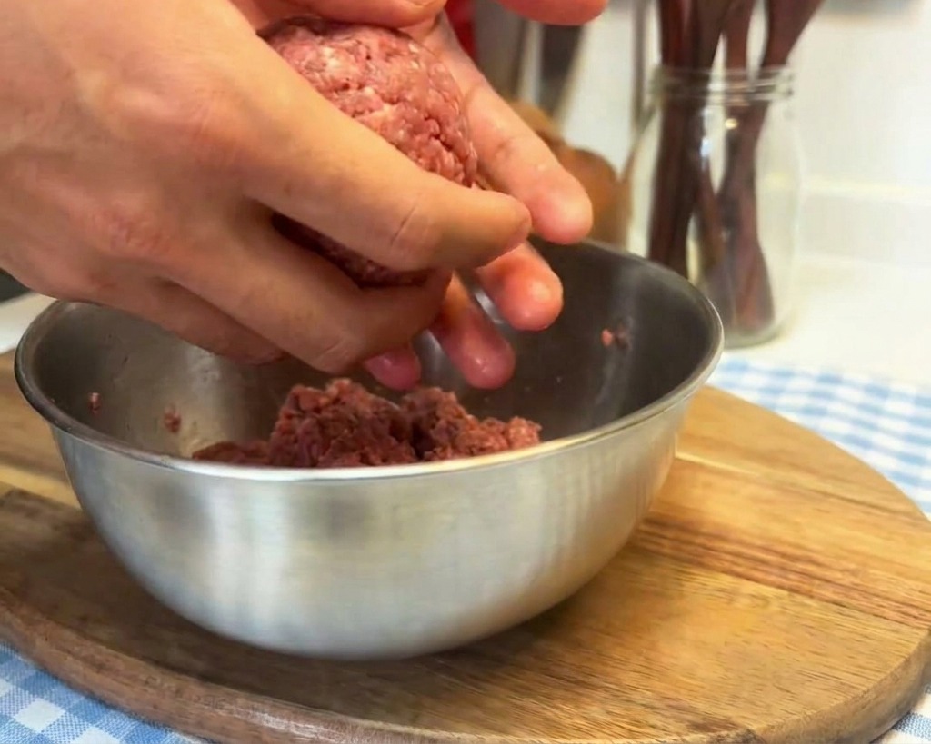 Mains travaillant une boule de bœuf cru en la frappant dans la paume pour raffermir la texture.