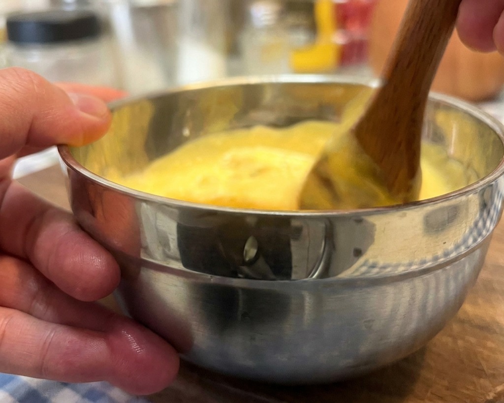 Une main mélangeant une sauce burger onctueuse de couleur orangée avec une cuillère en bois.