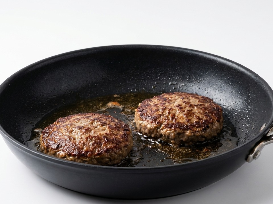 Deux steaks de bœuf retournés dans une poêle, montrant une croûte brune foncée et croustillante.