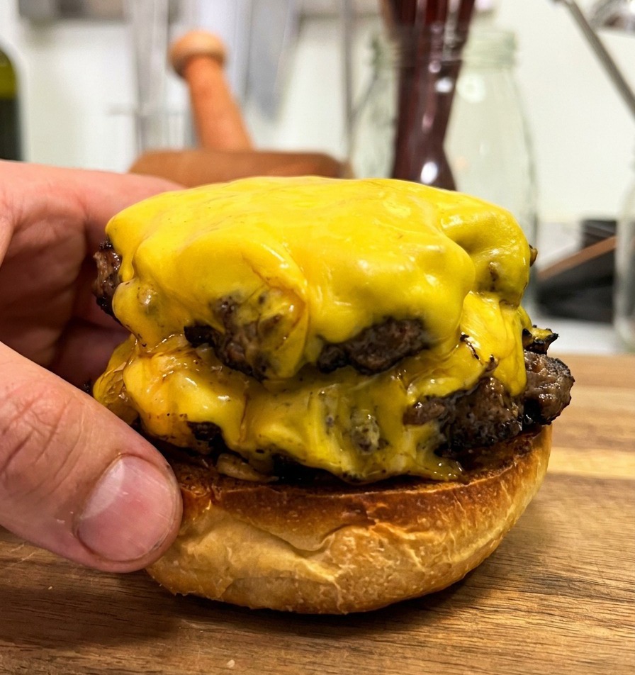 Deux steaks de bœuf superposés avec du fromage fondu sur un pain du bas, montrant la viande juteuse.