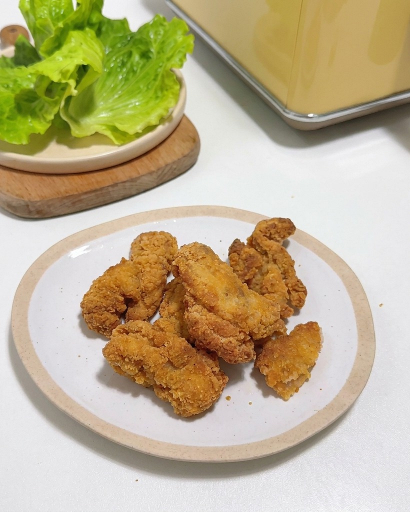 Morceaux de poulet frit croustillants empilés sur une petite assiette blanche à côté de feuilles de laitue fraîche.