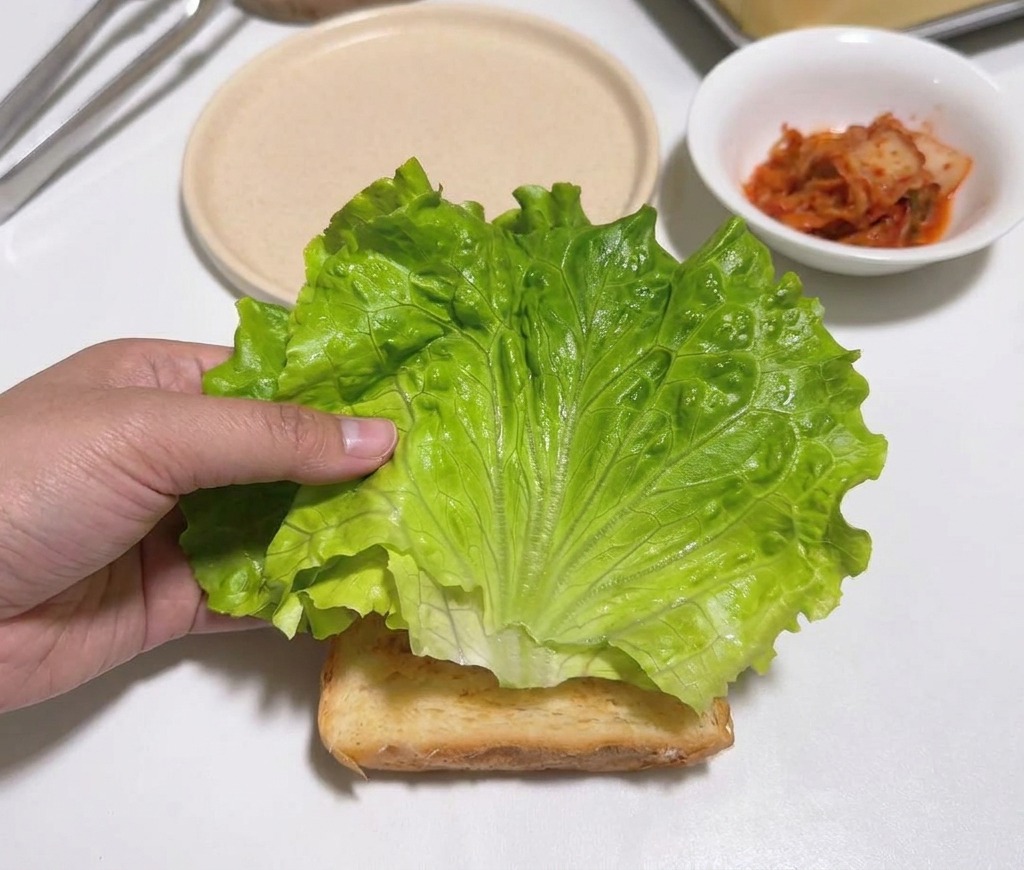 Une main plaçant une feuille de laitue verte croquante sur une tranche de pain grillé.