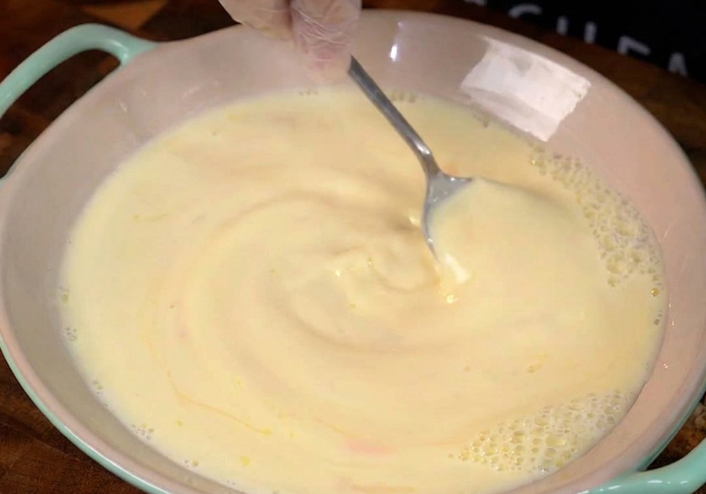 Mélange dœufs et de lait fouetté dans un bol en céramique rose.