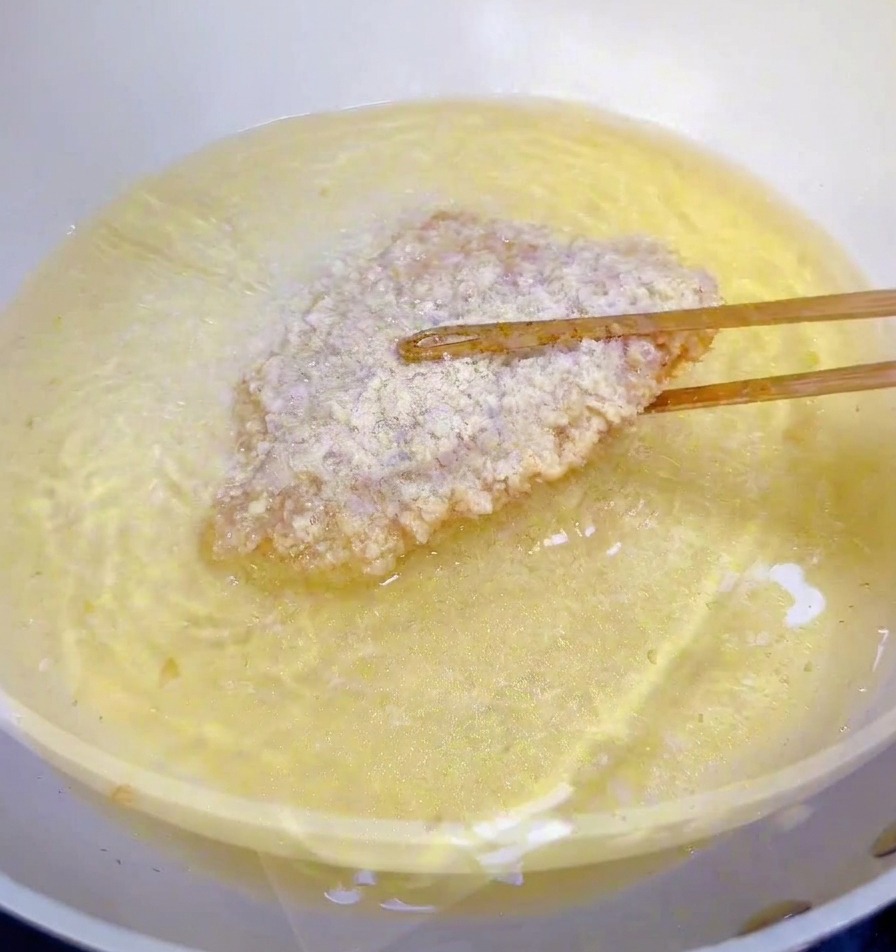 Un filet de poulet pané plongé dans une poêle dhuile chaude avec des baguettes en bois.