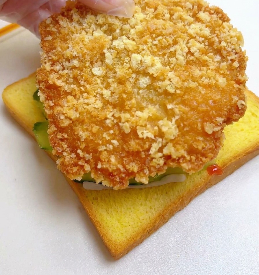 Une main posant le filet de poulet frit sur les concombres.