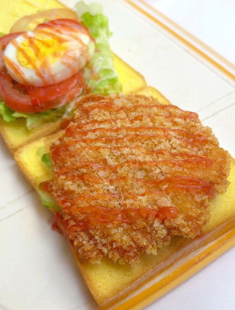 Filet de poulet pané sur le pain recevant un filet de ketchup et de moutarde au miel.